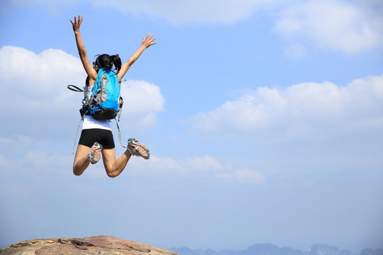 young asian woman hiker jumping mountain peak cliff