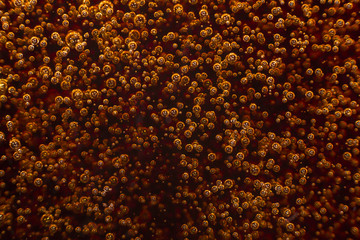 Macro black bubbles on glass wall of cola rise up