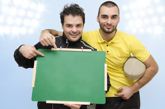 Rugby player and coach smiling, holding empty blackboard