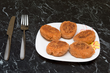 cutlet, knife and  fork on  white plate on  marble table. Photo