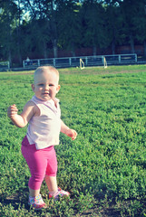 One-year-old girl baby on the walk on green grass