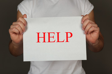 Sheet of paper with Help sign in male hands on dark background