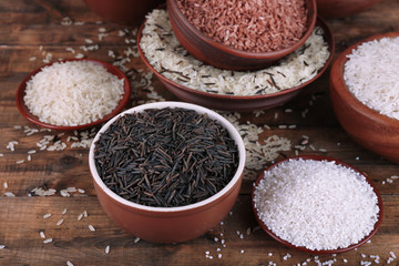 Different kinds of rice in bowls on wooden background