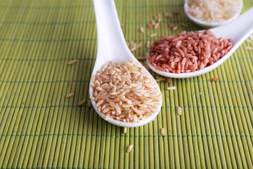 Different types of rice in spoons on bamboo background