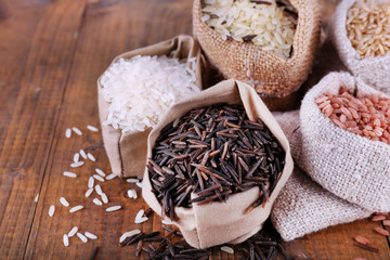 Different types of rice in sacks on wooden background