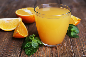 Glass of orange juice with oranges on wooden table close up