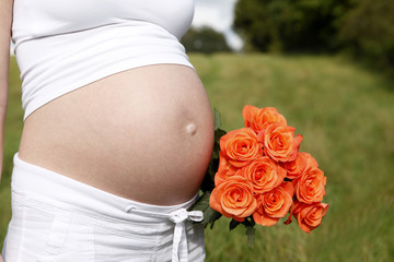 Pregnant woman outdoor with orange tulips in her hands