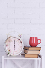 Interior design with alarm clock, stack of books and pink cup