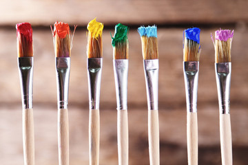 Brushes with colorful paints on old wooden background
