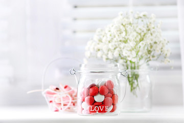 Sweet candies in jar with flowers on windowsill background