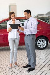 car dealer explaining sales contract to young woman