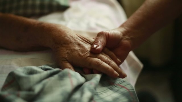 Elderly person holding hands as she lays down in bed