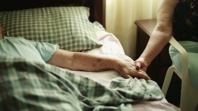 Elderly Woman lying down and holding another woman's hands