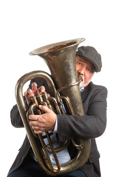 A man wearing a hat and blazer playing a vintage silver Tuba isolated on a white background