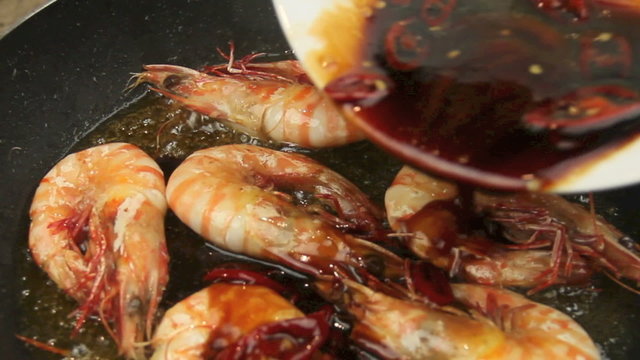Chili marinade poured on shrimps in a hot frying pan.