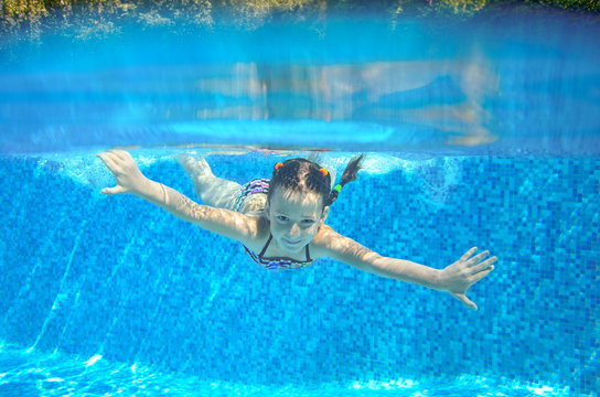 Happy girl swims in pool underwater, active kid swimming