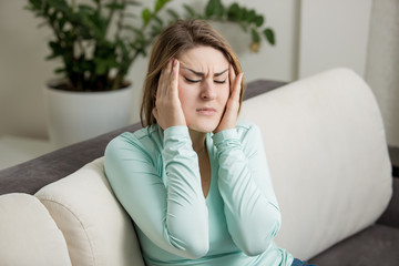 woman sitting on sofa and suffering from head ache