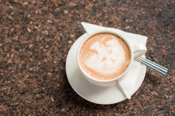 Cup of coffee with spoon on marble dark table.