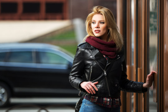 Young fashion blond woman in leather jacket at the mall door