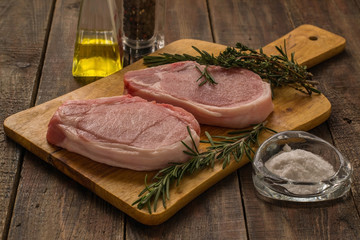 Raw pork steak with thyme and rosemary on a cutting board