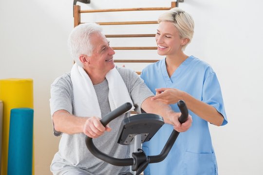 Senior man doing exercise bike with therapist - Powered by Adobe