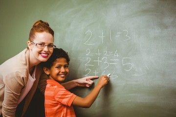 Teacher assisting boy to write on blackboard in classroom