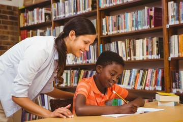 Teacher assisting mixed race boy with homework in library
