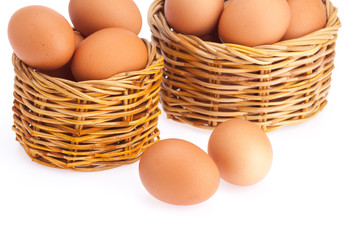 Wicker basket with eggs are packed to overflowing . Eggs are laid on a white background.