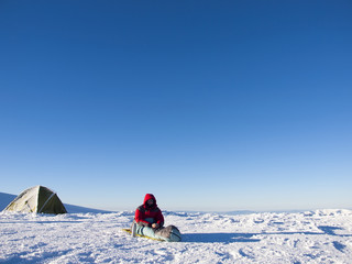 A man sits in a sleeping bag near the tent.