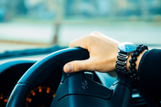 Male hand with bracelet and watch driving a car