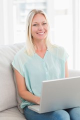 Happy woman using laptop while sitting on sofa