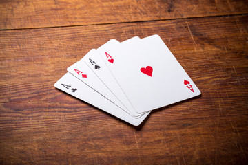 A group of four playing card aces on a stained oak wooden table.