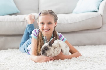 Happy girl with rabbit lying on rug in living room