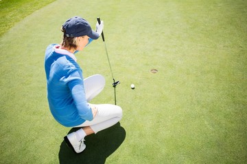 Focused lady golfer kneeling on the putting green