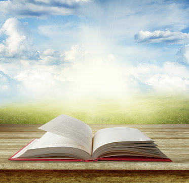 Open book on wooden table and bright sky spring scene