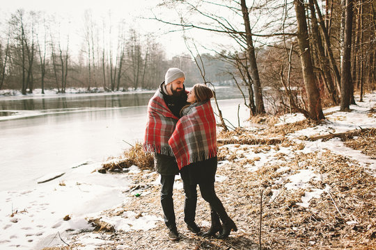 Couple looking each other near winter lake under plaid