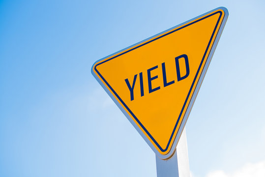 A yellow yield sign against a blue sky background