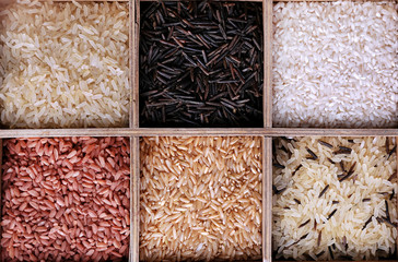Different types of rice in box on wooden background