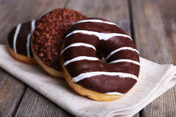 Delicious donuts with icing on napkin on wooden background