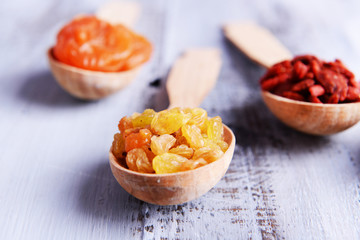 Dried fruits in spoons on color wooden table background