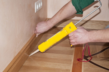 Carpenter on work putting wood parquet skirting board with glue