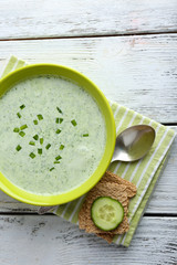 Cucumber soup in bowl on color wooden table background