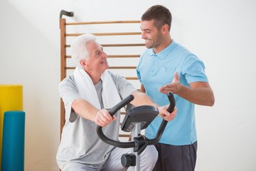 Senior man doing exercise bike with his trainer