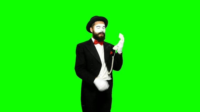 Man mime hears the ring of telephone and answers on green screen