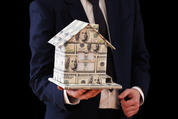 Model of house made of money in male hand on dark background