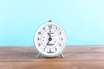 Alarm clock on wooden table on blue background