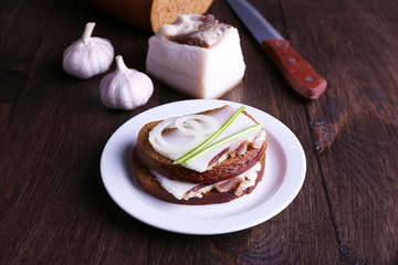 Sandwiches with lard on plate and garlic on wooden background