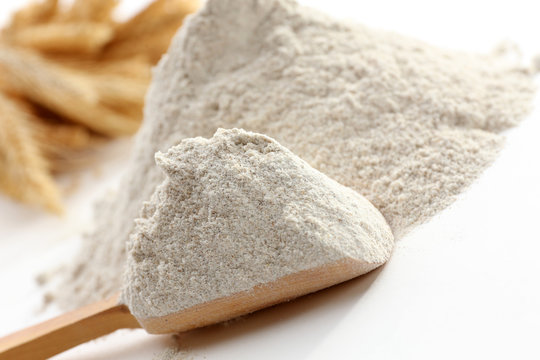 Heap of flour with wooden spoon and ears close up
