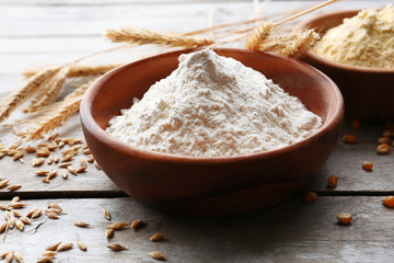Flour in bowls with grains on wooden background