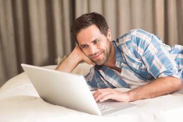 Handsome man relaxing on his bed with laptop